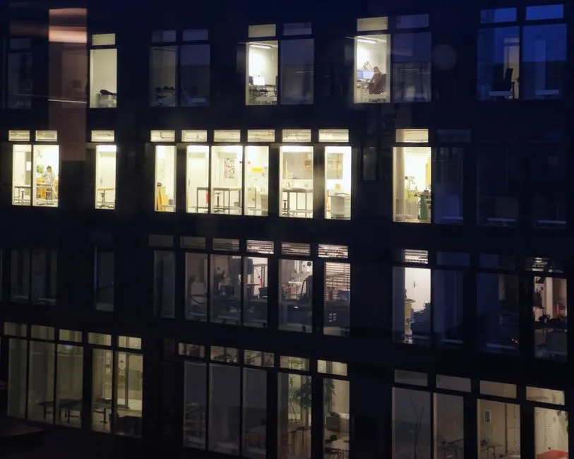 Office building exterior with lit windows at night, showing various workspaces.