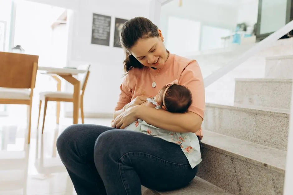 Woman smiling and cradling baby on stairs indoors, portraying warmth and family bonding.