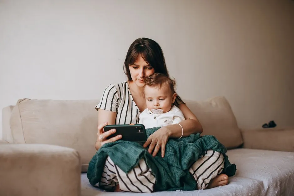 A mother and her baby boy bonding and looking at a smartphone while sitting on a comfortable sofa indoors.