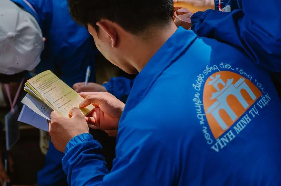 A volunteer reads a booklet at a community gathering, captured candidly in a lively setting.